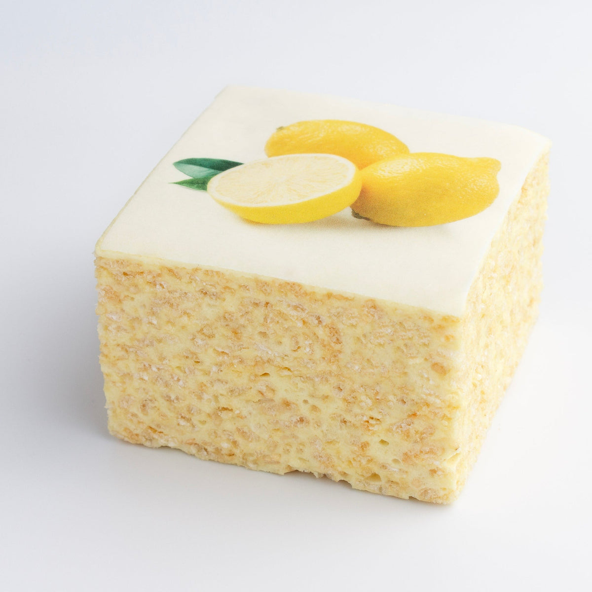 The Crispery Tropical Fruit Lemon Crispycake on a grey background, with printed lemons on the white top and pale crispy rice sides