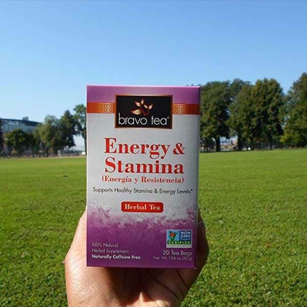 Hand holding a Bravo Tea Energy & Stamina box in front of a grassy park