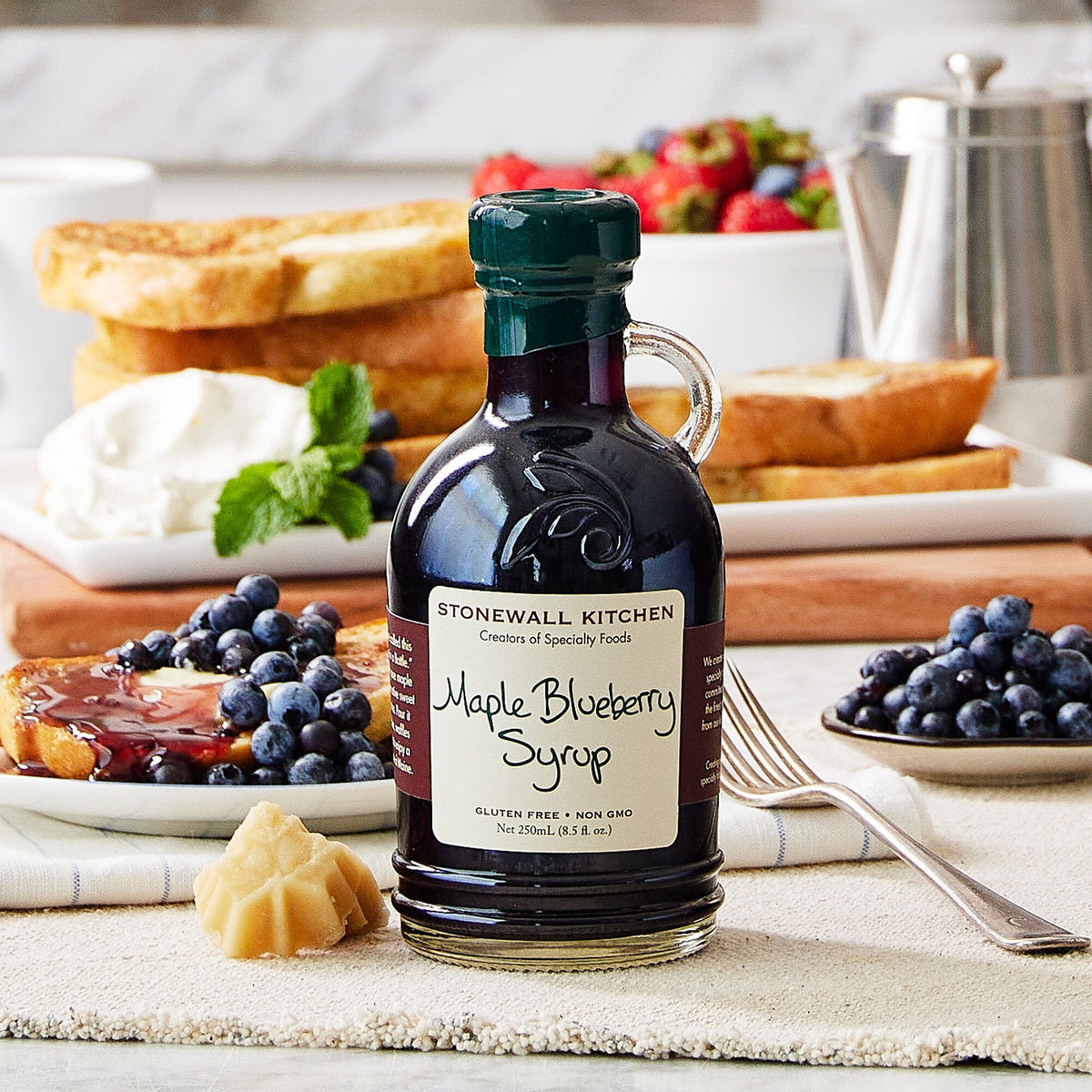 Bottle of Stonewall Kitchen Maple Blueberry Syrup on a breakfast table with French toast, fresh blueberries and strawberries
