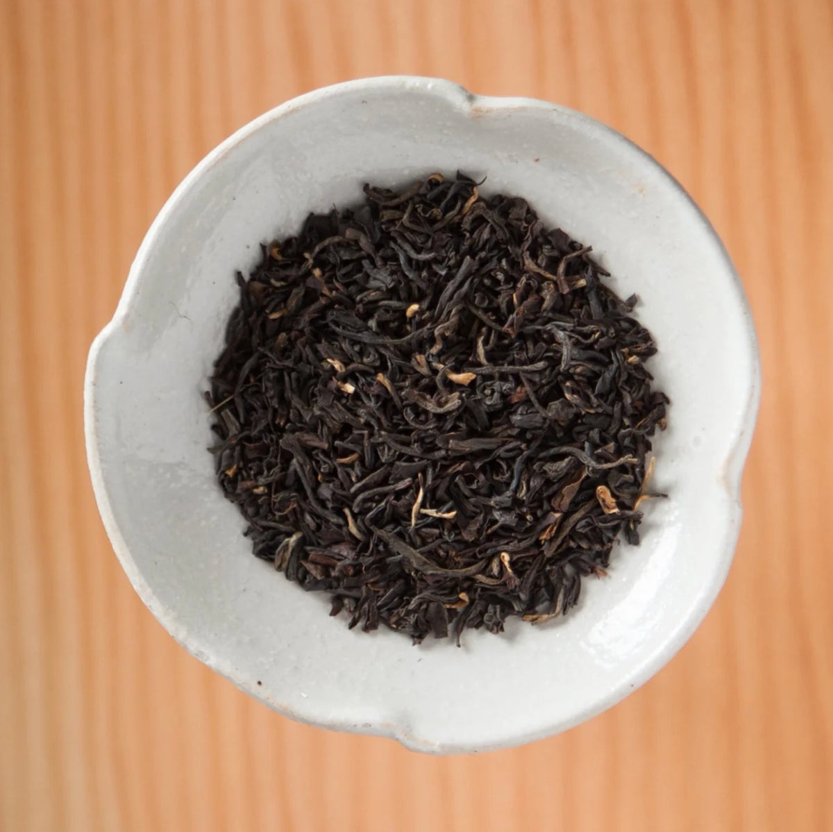 Dry Coastal Breakfast tea blend in a bowl on a wooden table, showing the loose leaves and herbs inside the tea bags