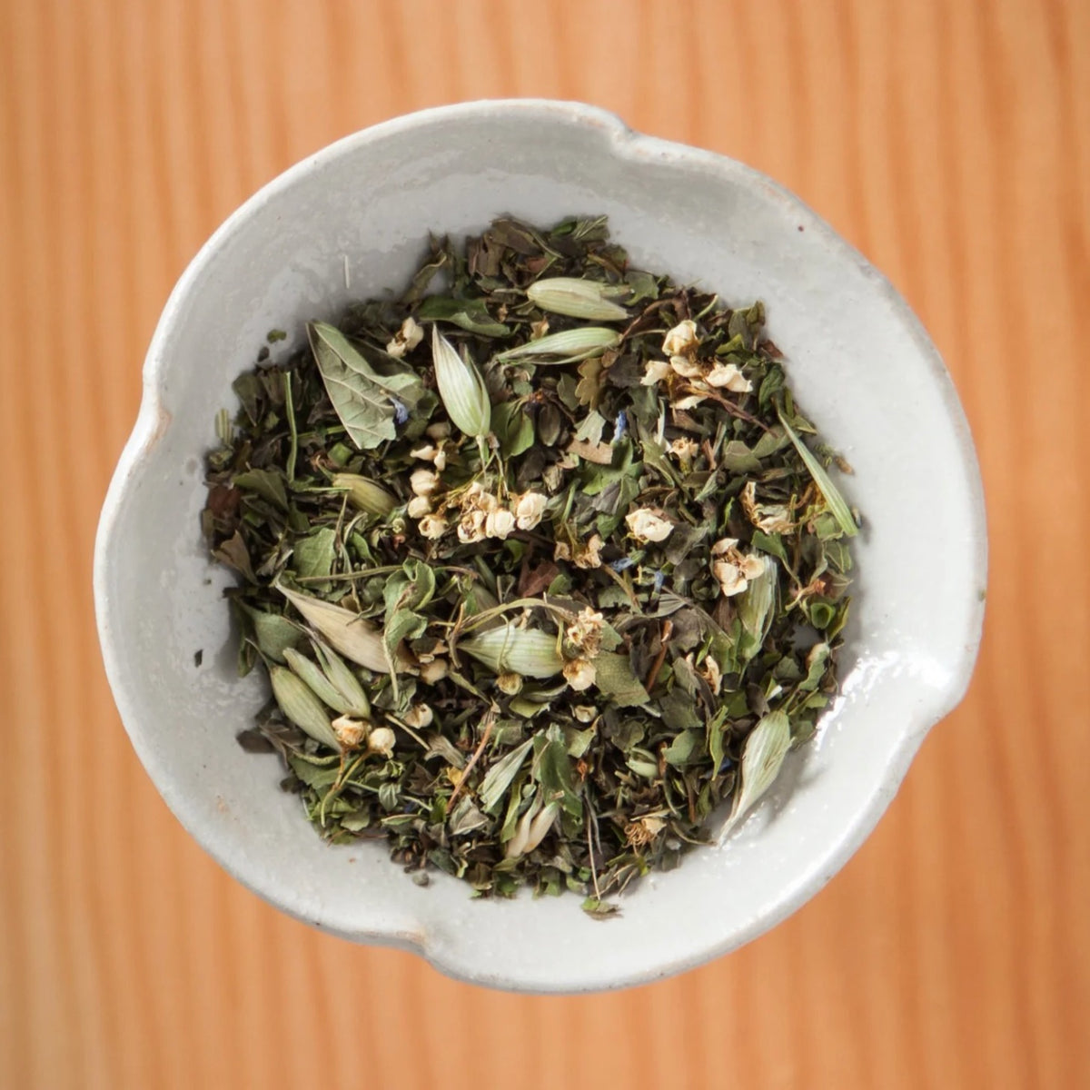 Dry Peace of Mind tea blend in a bowl on a wooden table, showing the loose leaves and herbs inside the tea bags
