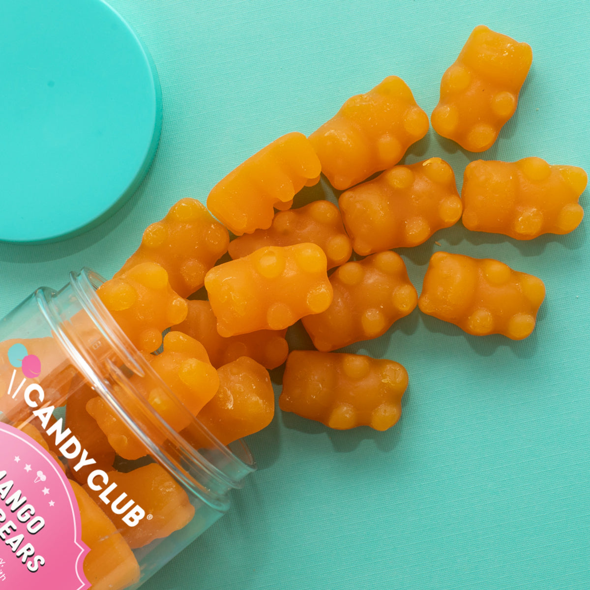 Orange Mango Chili gummy bears spilling from a tipped Candy Club cup beside its teal lid