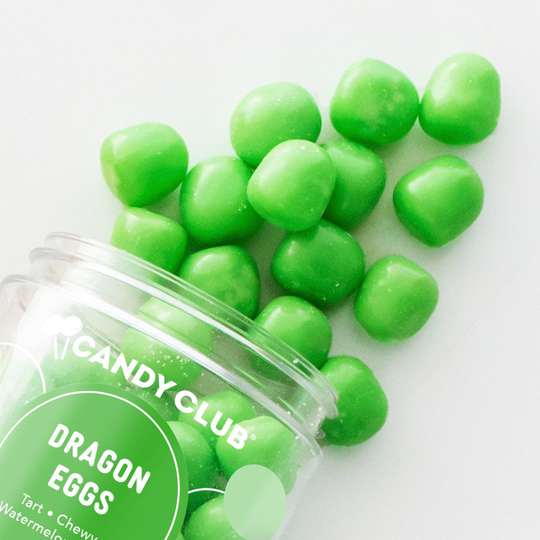 Green Dragon Eggs candies spilling from a tipped Candy Club cup onto a light gray surface