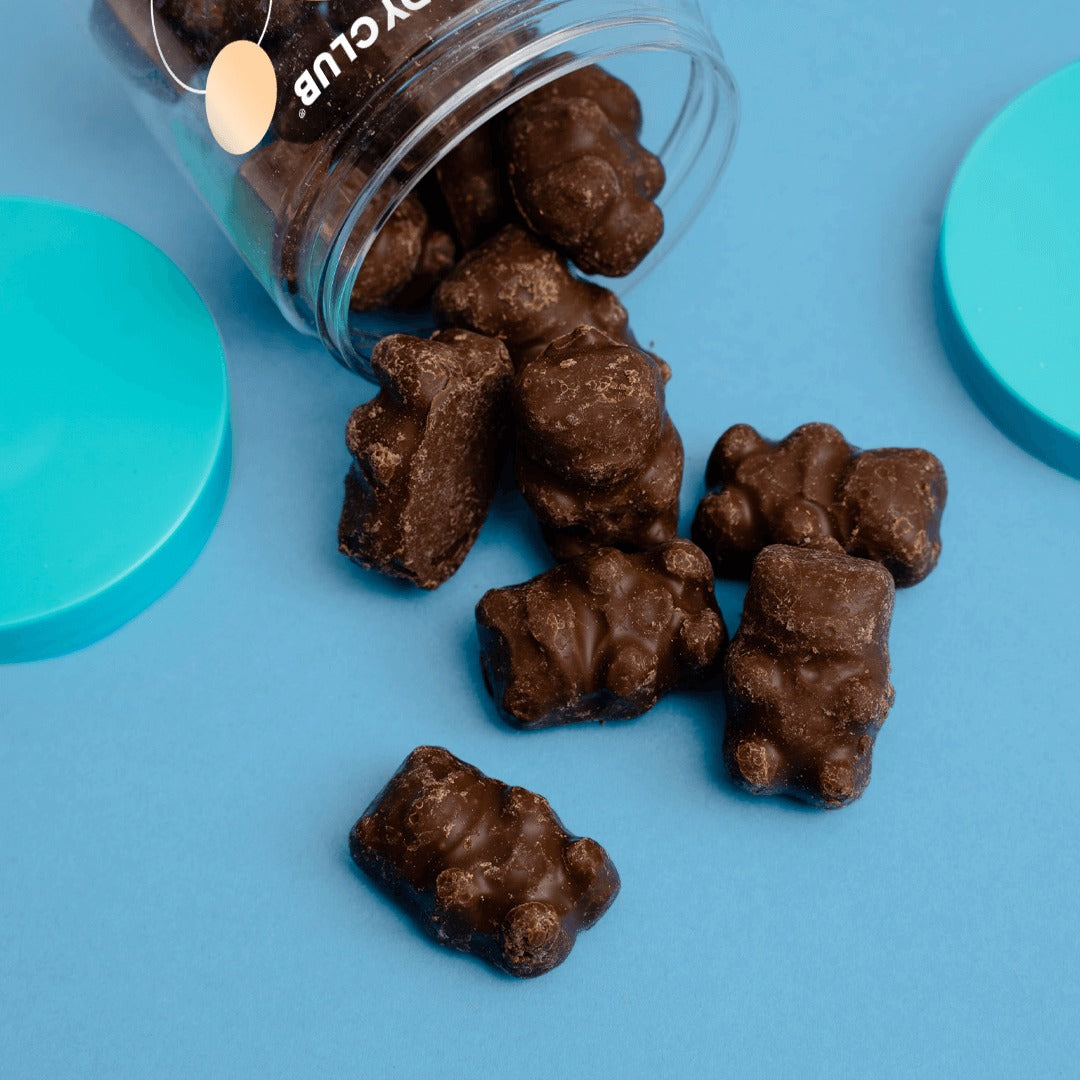 Candy Club Choco Bears spilling from a tipped cup onto a blue surface, showing milk chocolate-coated gummy bear shapes
