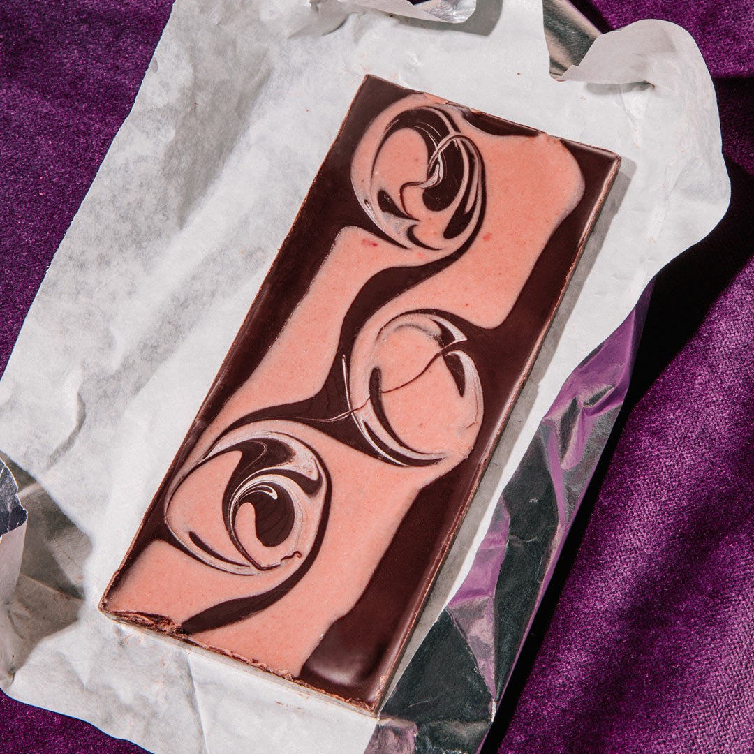 Unwrapped Raaka Strawberry Swirl bar on its paper and foil wrapper, showing pink strawberry white chocolate swirled through dark chocolate