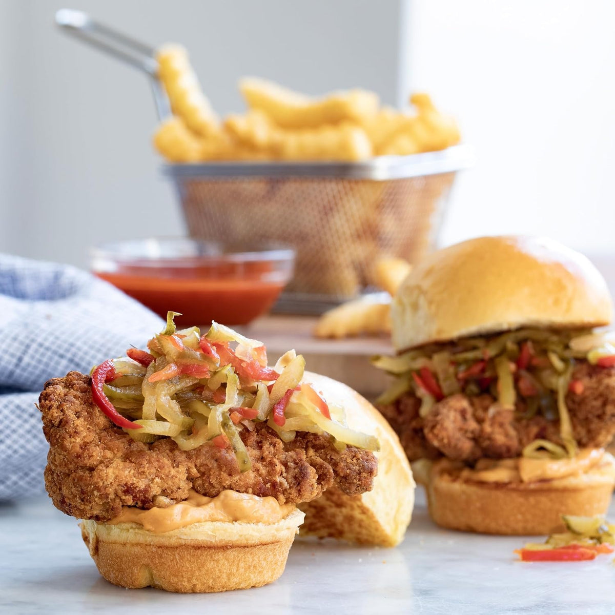 Fried chicken sliders topped with Stonewall Kitchen Pickle Slaw, with a basket of crinkle-cut fries behind them