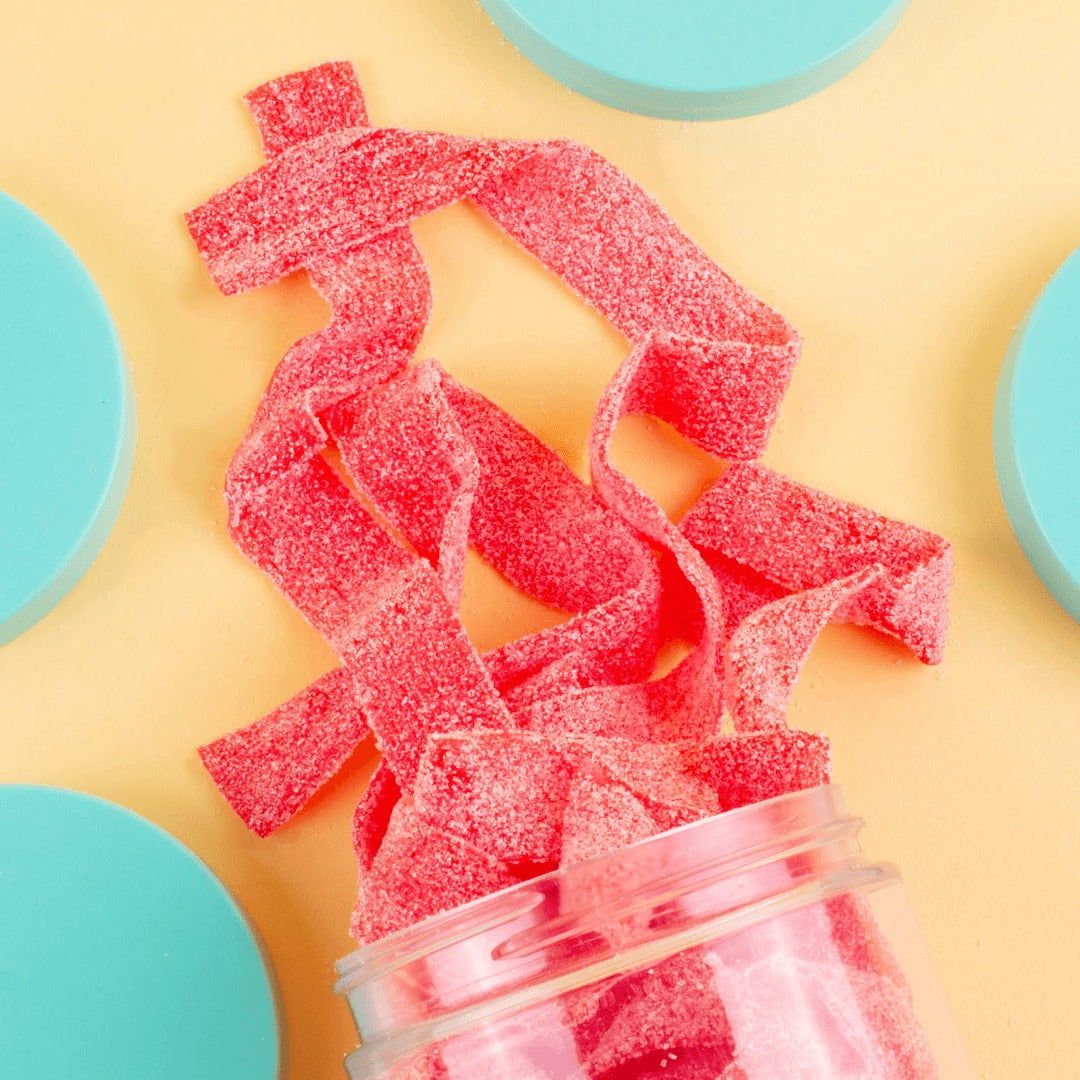 Long sugar-sanded red strawberry sour belts pulled from the Candy Club cup on a yellow surface