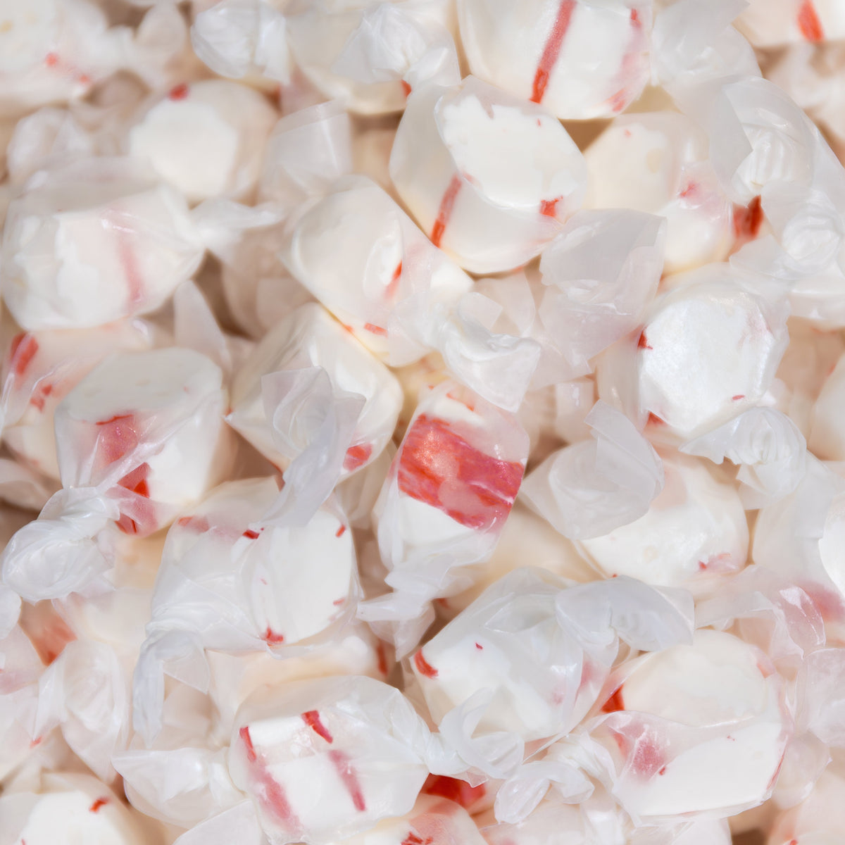 Close-up of a pile of wrapped Sweet's Peppermint taffy pieces, white with red stripes