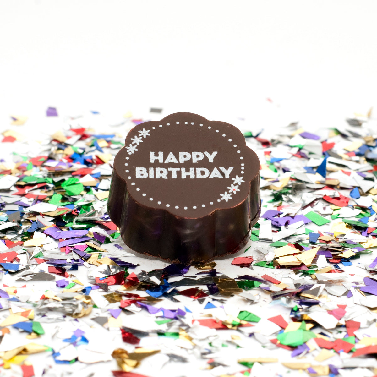Close-up of a Chouquette Birthday chocolate with HAPPY BIRTHDAY in white block letters and stars, on colorful confetti