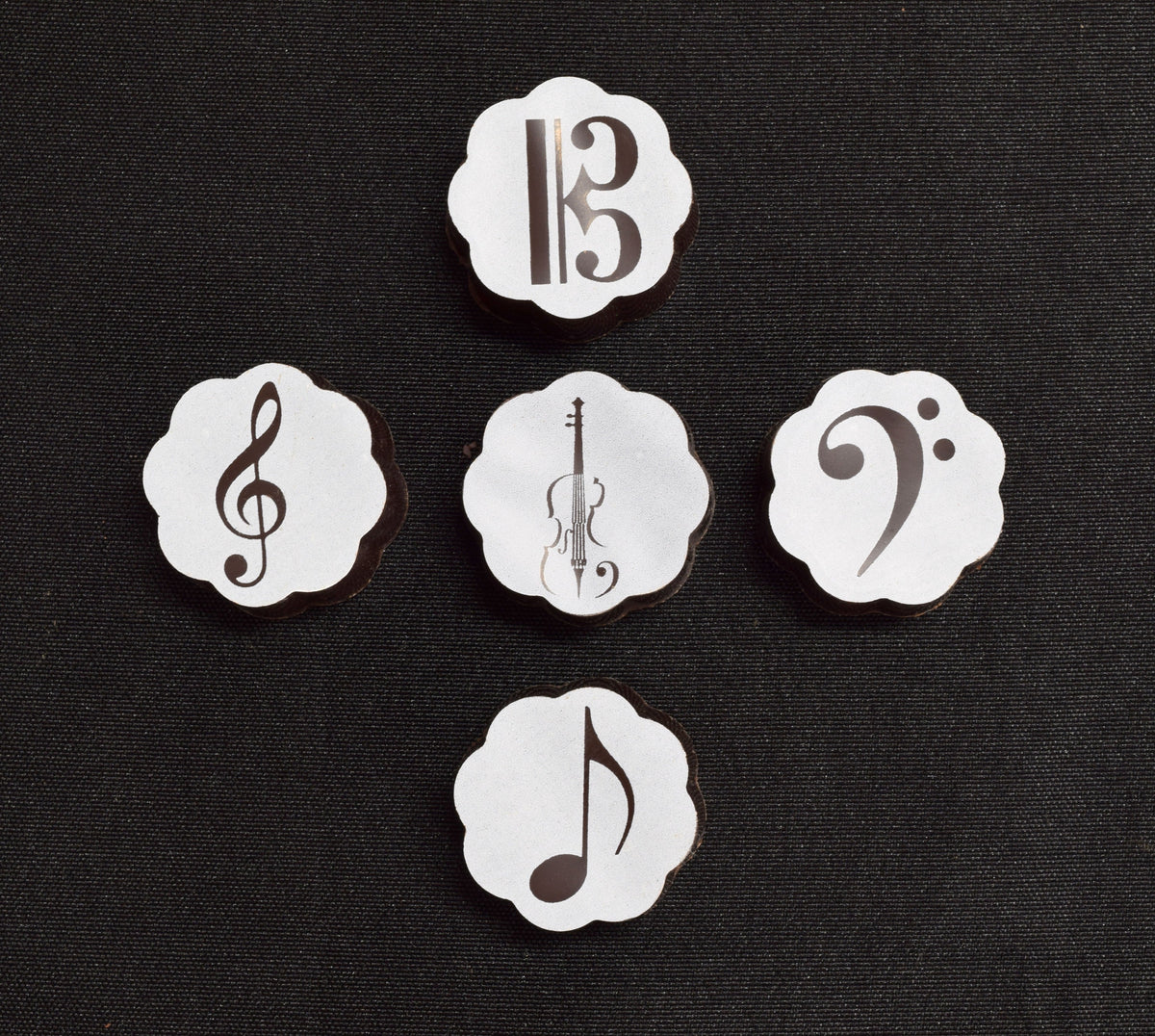 Five Chouquette A Sweet Song chocolates on black fabric: alto clef, treble clef, string instrument, bass clef and eighth note