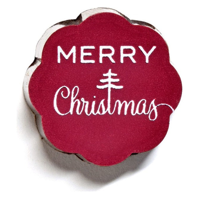 Close-up of one Chouquette Merry Christmas chocolate caramel with white lettering and a small tree on a red scalloped top