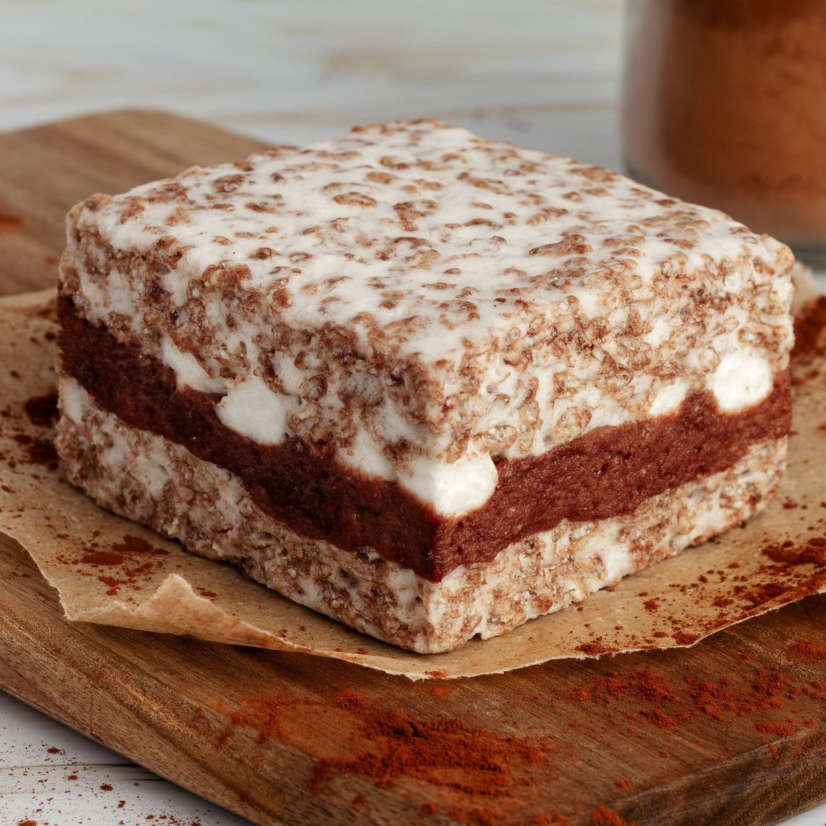 The Crispery Cocoa Concoction Crispycake on parchment and a wooden board, showing the chocolate layer through the middle of the cocoa cereal treat