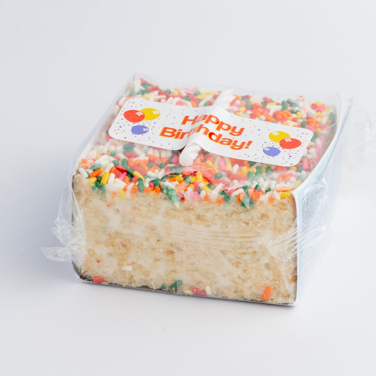 The Crispery Happy Birthday Crispycake in its clear cellophane wrap, with a balloon-print Happy Birthday label over the rainbow sprinkles