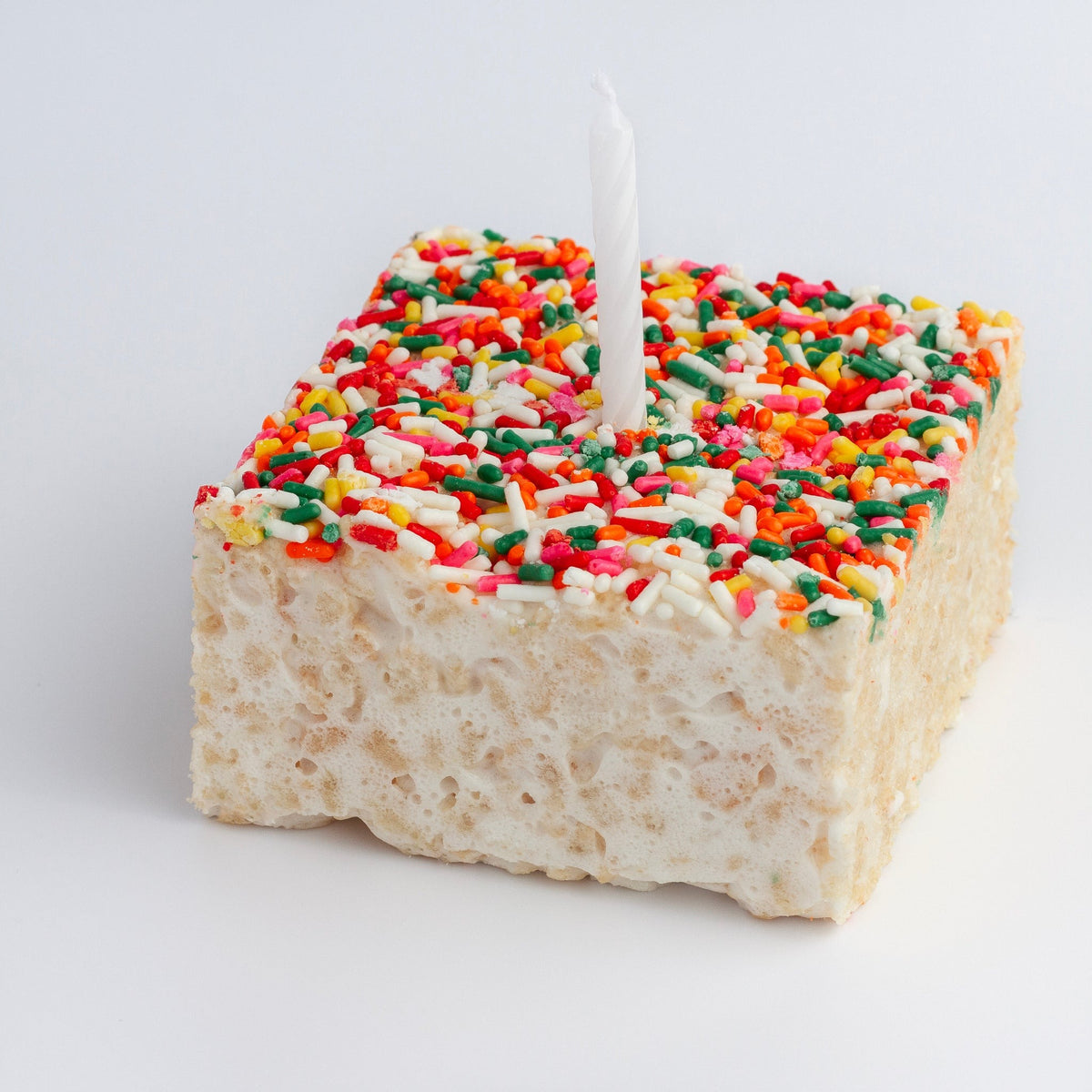 The Crispery Happy Birthday Crispycake unwrapped, rainbow sprinkles on top with a white birthday candle standing in it