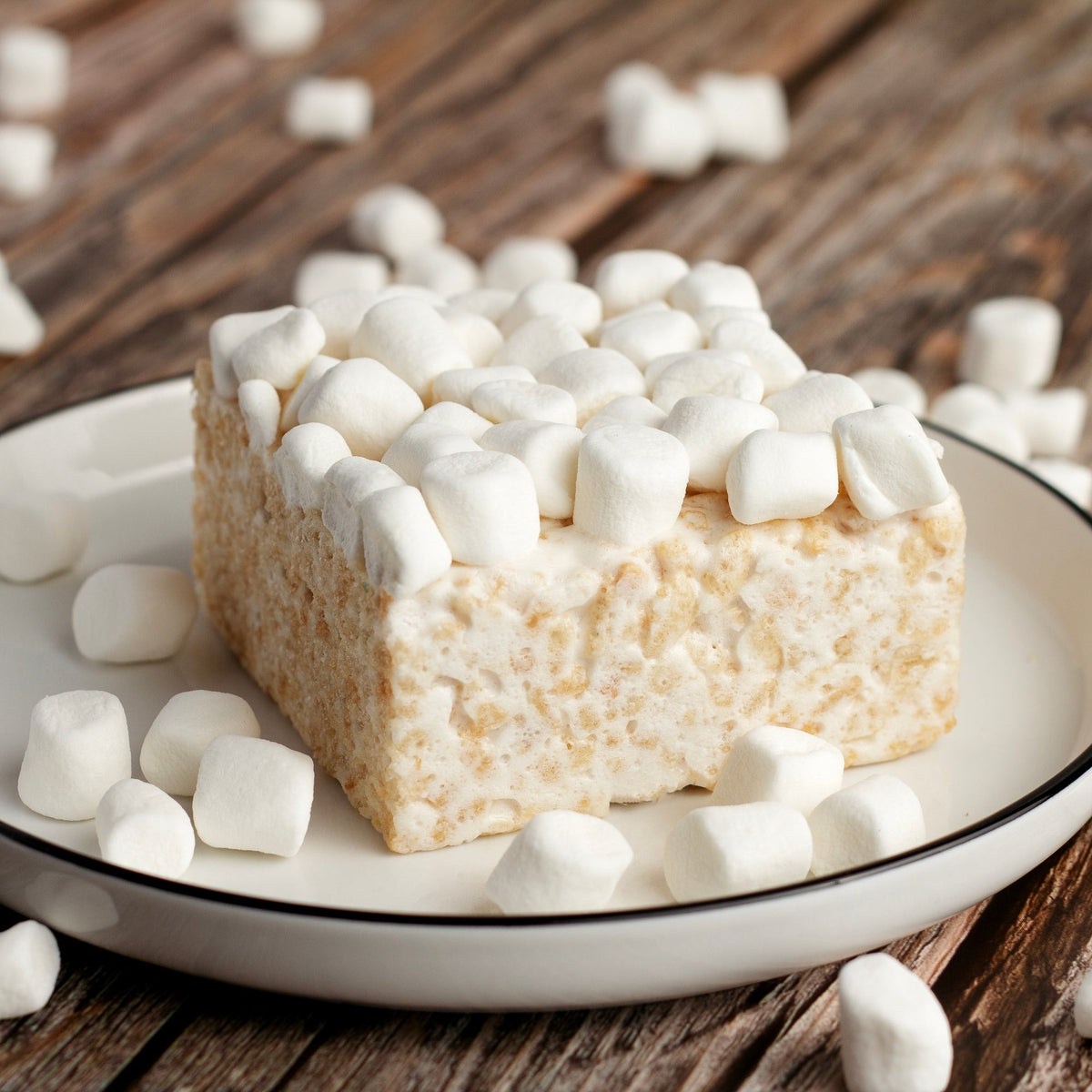 Mini Marshmallow Crispycake on a white plate with loose mini marshmallows on a wooden table