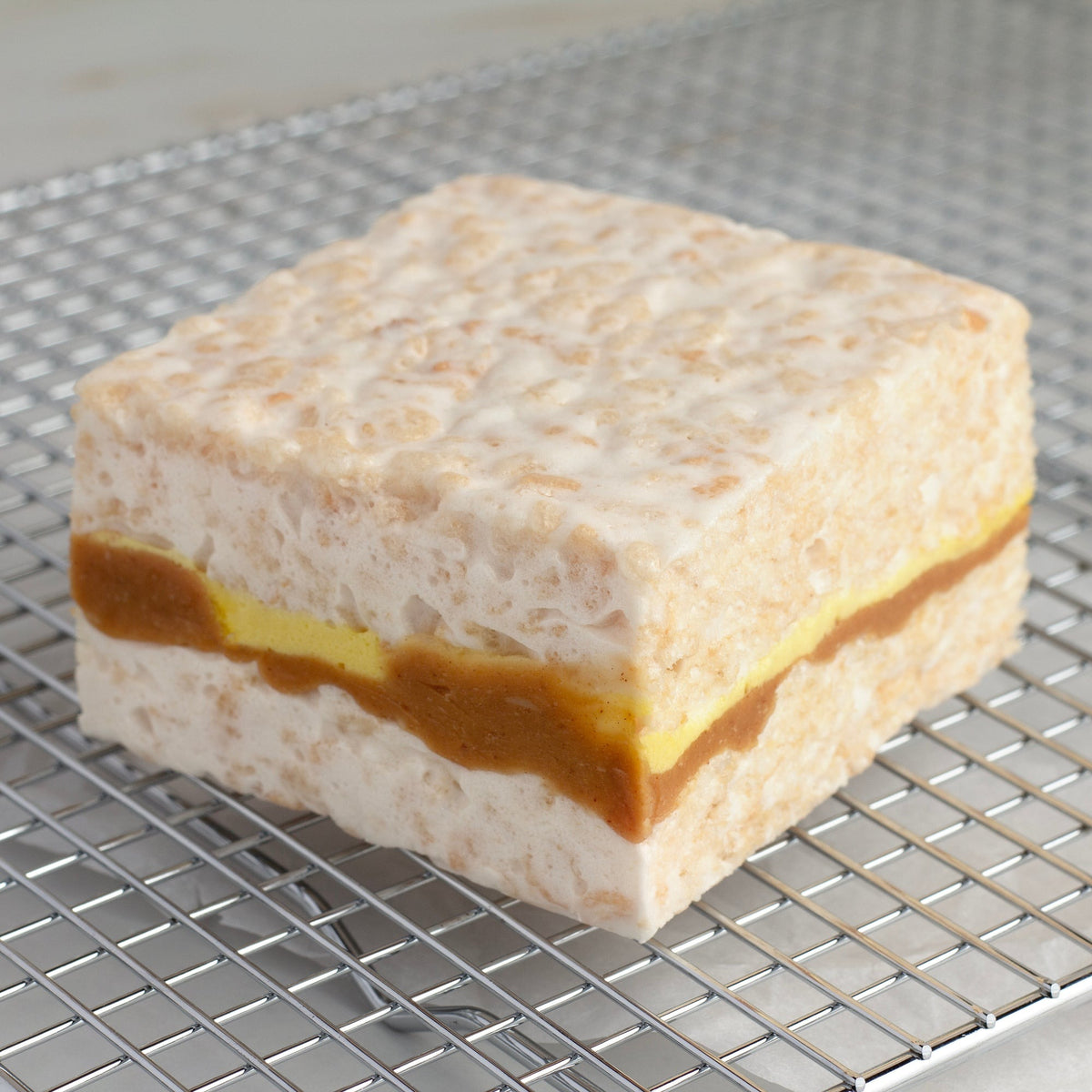 Peanut Butter & Banana Crispycake on a wire cooling rack, side view of the peanut butter and banana center layer