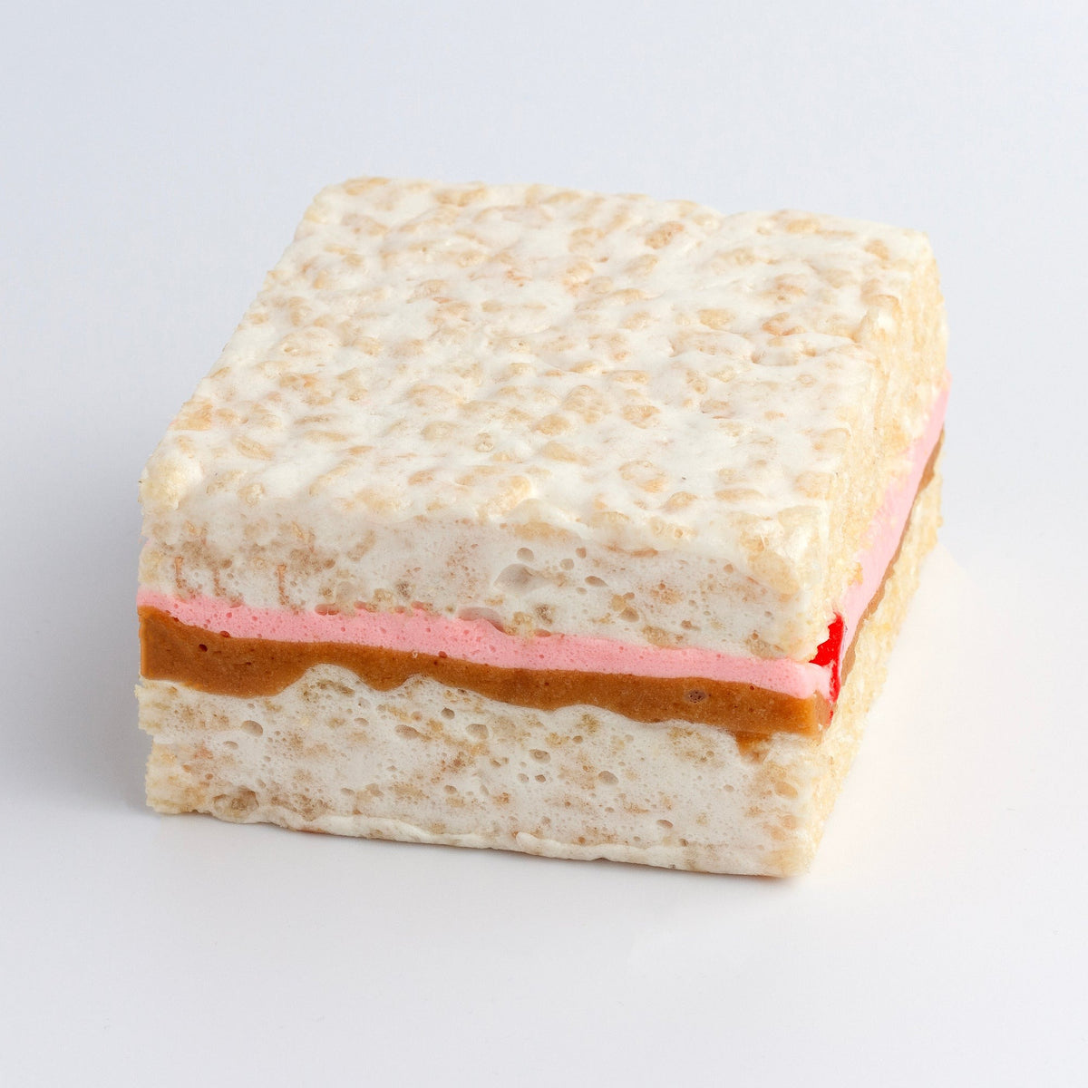 Peanut Butter & Jelly Crispycake on a white background showing a peanut butter layer and a pink jelly layer through the middle
