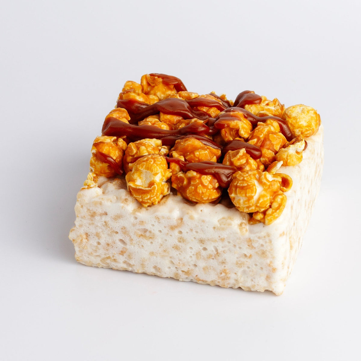 Popcorn Crunch Crispycake on a white background, topped with golden popcorn and a caramel-colored drizzle