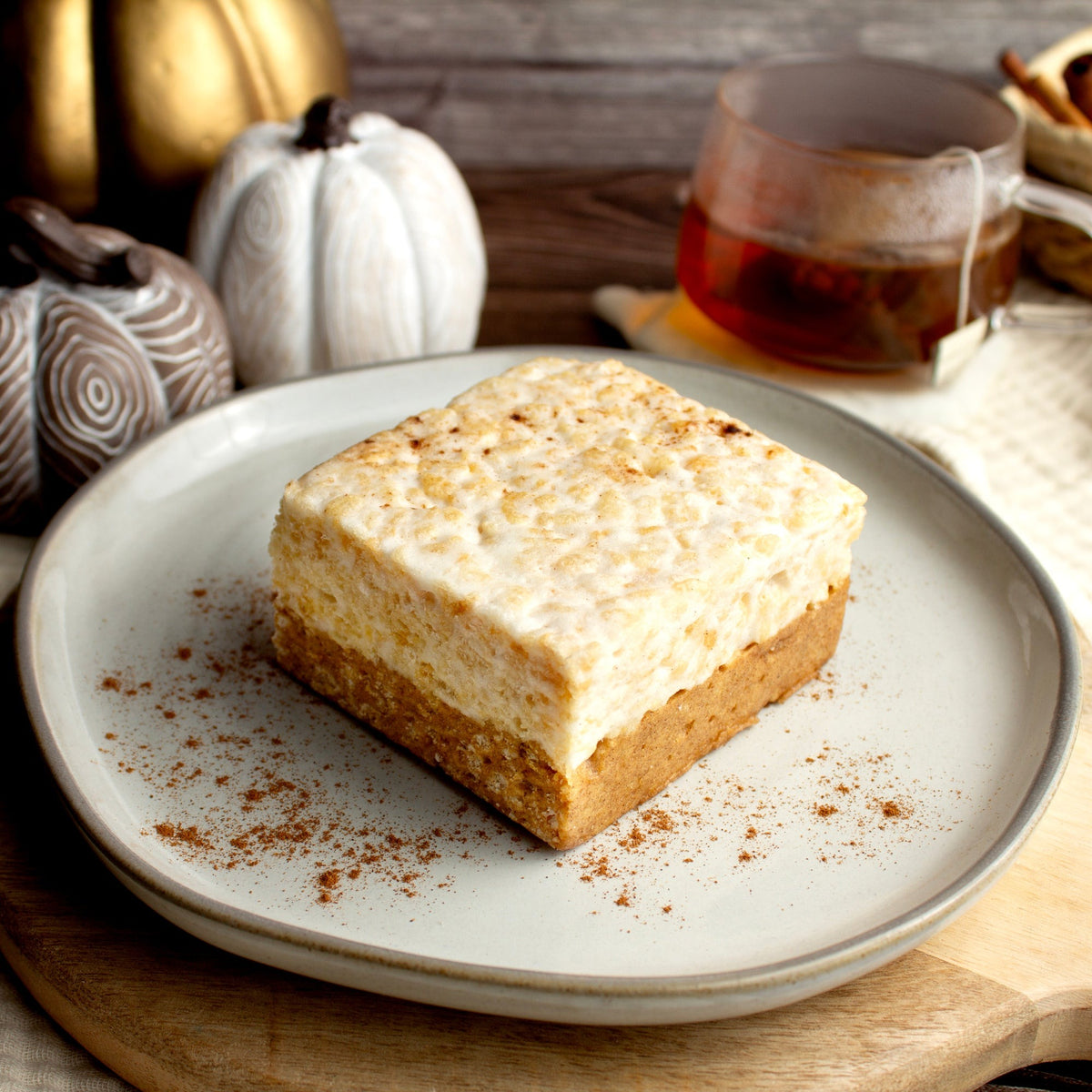 Pumpkin Spice Crispycake on a plate dusted with spice, with small pumpkins and a cup of tea