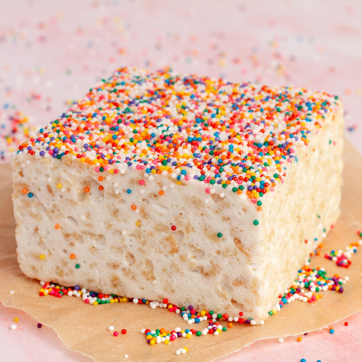 Rainbow Nonpareils Crispycake on parchment with loose nonpareils on a pink surface