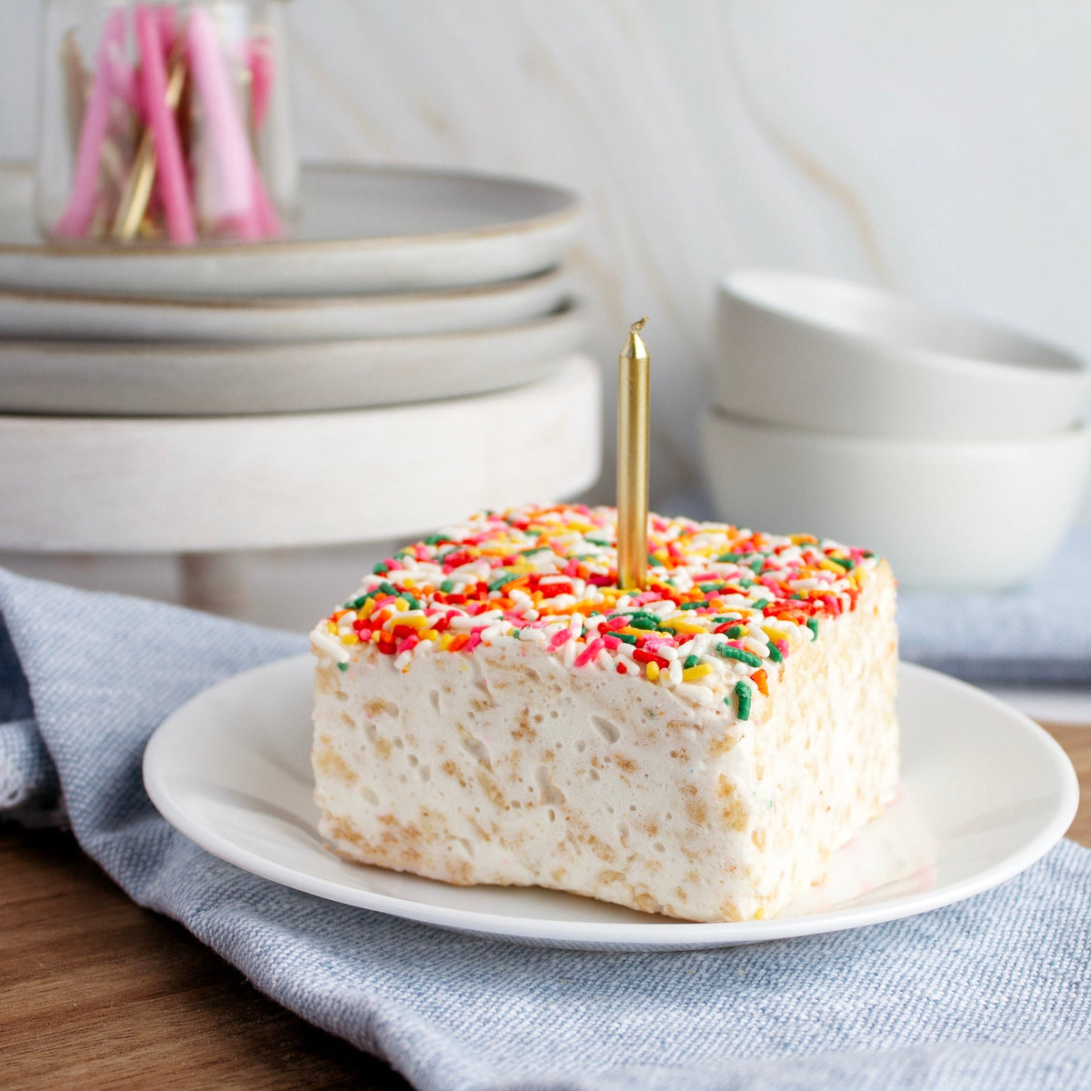 Rainbow Sprinkles Crispycake on a white plate with a gold birthday candle in the top