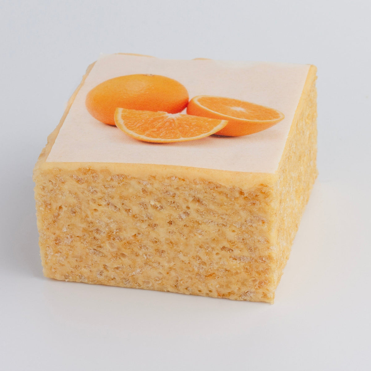 The Crispery Tropical Fruit Orange Crispycake on a grey background, with printed orange slices on top and crispy rice sides