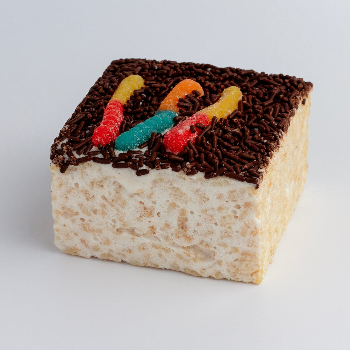 The Crispery Worms in Dirt Crispycake on a grey background, with three sour gummy worms on a layer of chocolate sprinkles