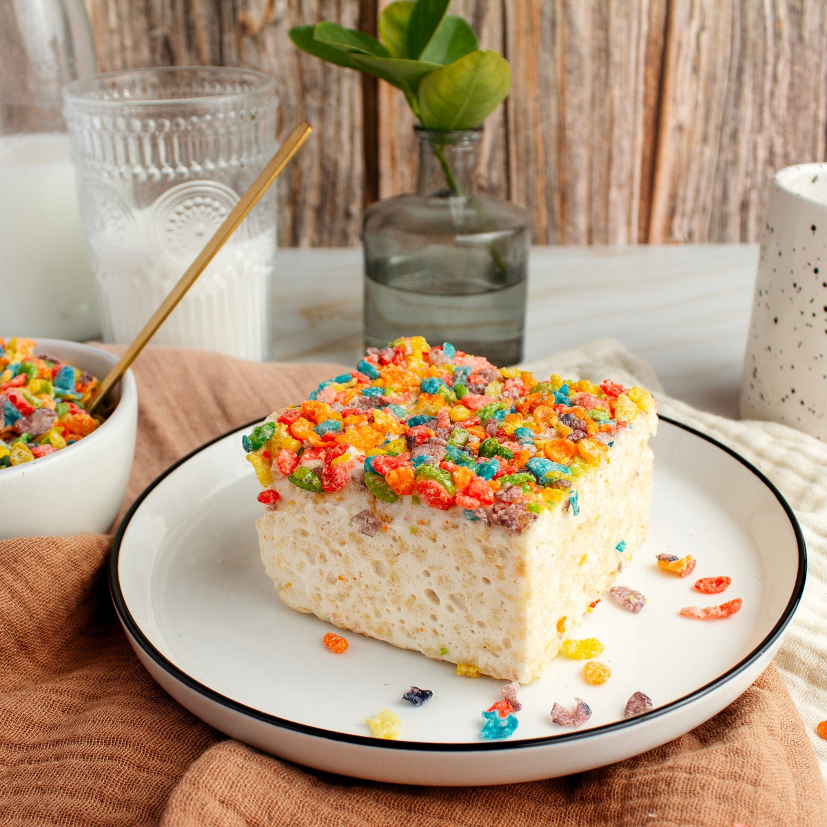 Fruity Crispies Crispycake on a white plate beside a bowl of fruity cereal and a glass of milk