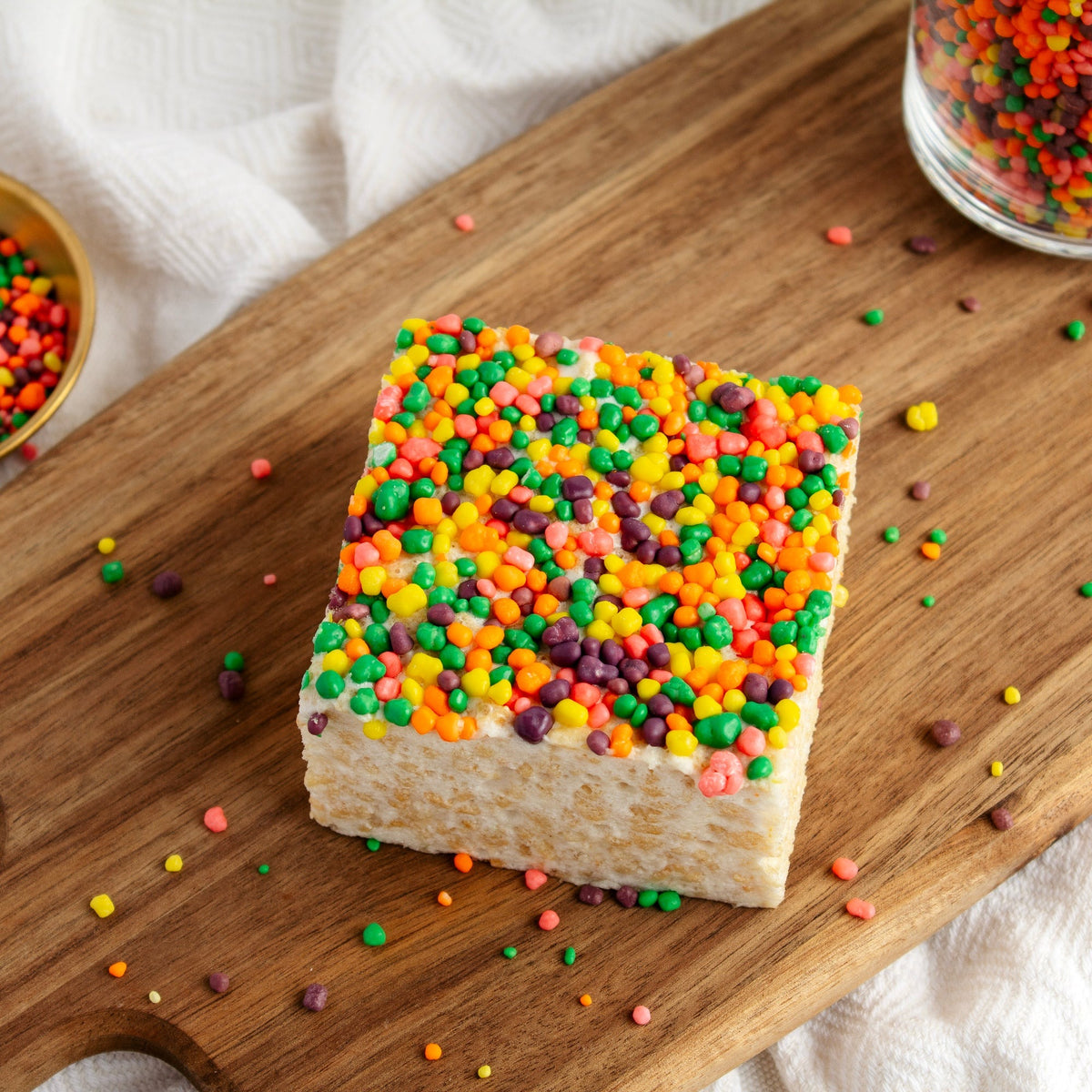 Nerdtastic Crispycake on a wooden serving board with loose colorful candies scattered around it