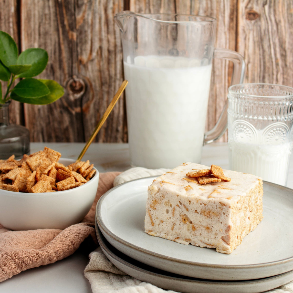 Toasted Cinnamon Crispy Crispycake on stacked plates with cinnamon cereal squares on top, beside a bowl of cereal and a pitcher of milk