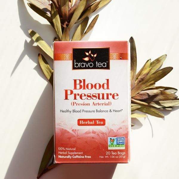 Hand holding a box of Bravo Blood Pressure Herbal Tea in front of dried leaves