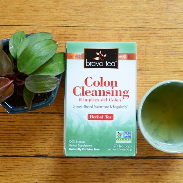 Bravo Colon Cleansing Herbal Tea box on a wooden table beside a potted plant and a cup of tea