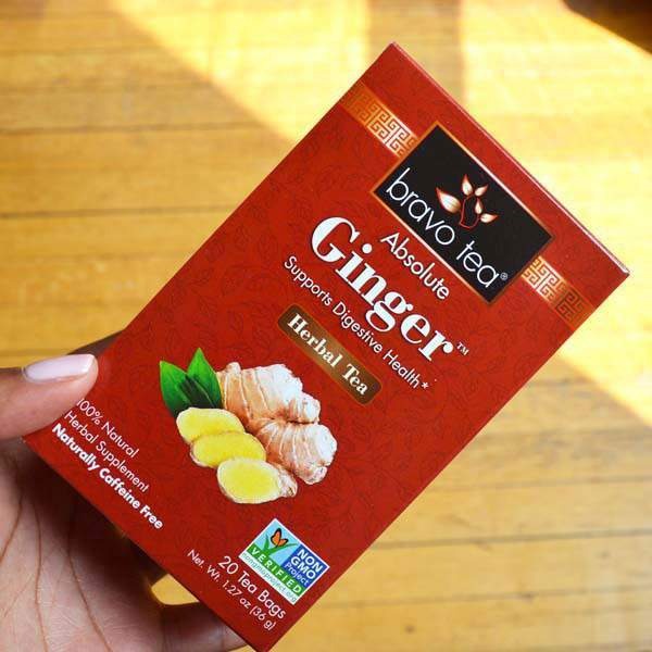 Hand holding a Bravo Tea Absolute Ginger box in sunlight above a wooden floor