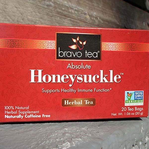 Bravo Tea Absolute Honeysuckle box on its side on a wooden step, front panel showing 20 tea bags and Net Wt. 1.06 oz