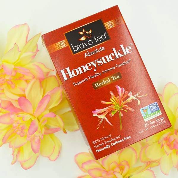 Bravo Tea Absolute Honeysuckle box with honeysuckle flower artwork, laid beside yellow and pink flowers