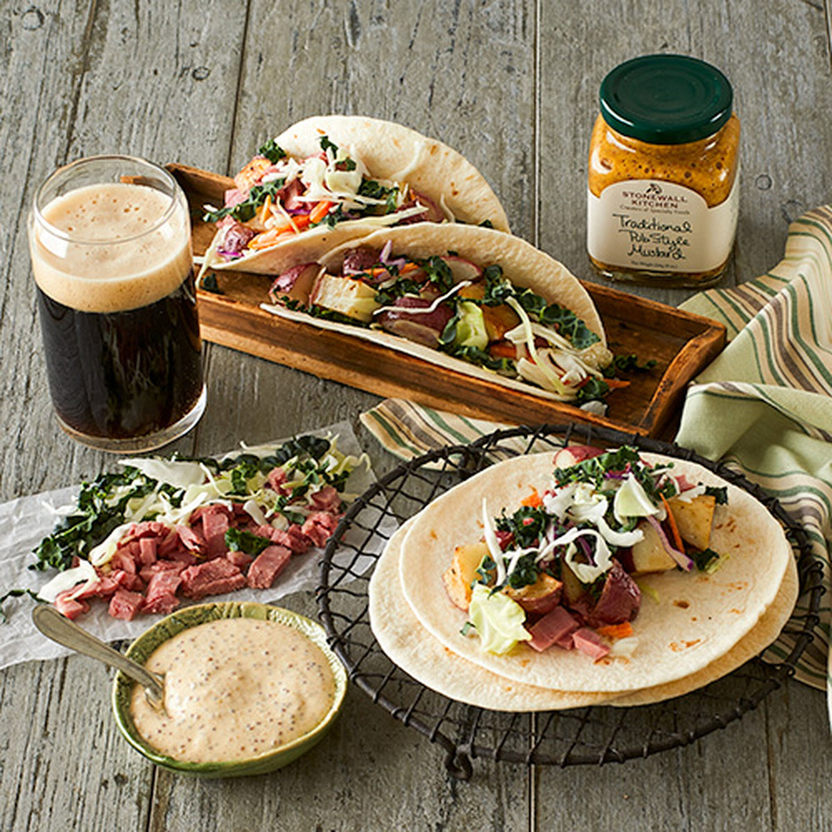 Jar of Stonewall Kitchen Traditional Pub Style Mustard on a wooden table beside corned beef and cabbage tacos and a glass of stout