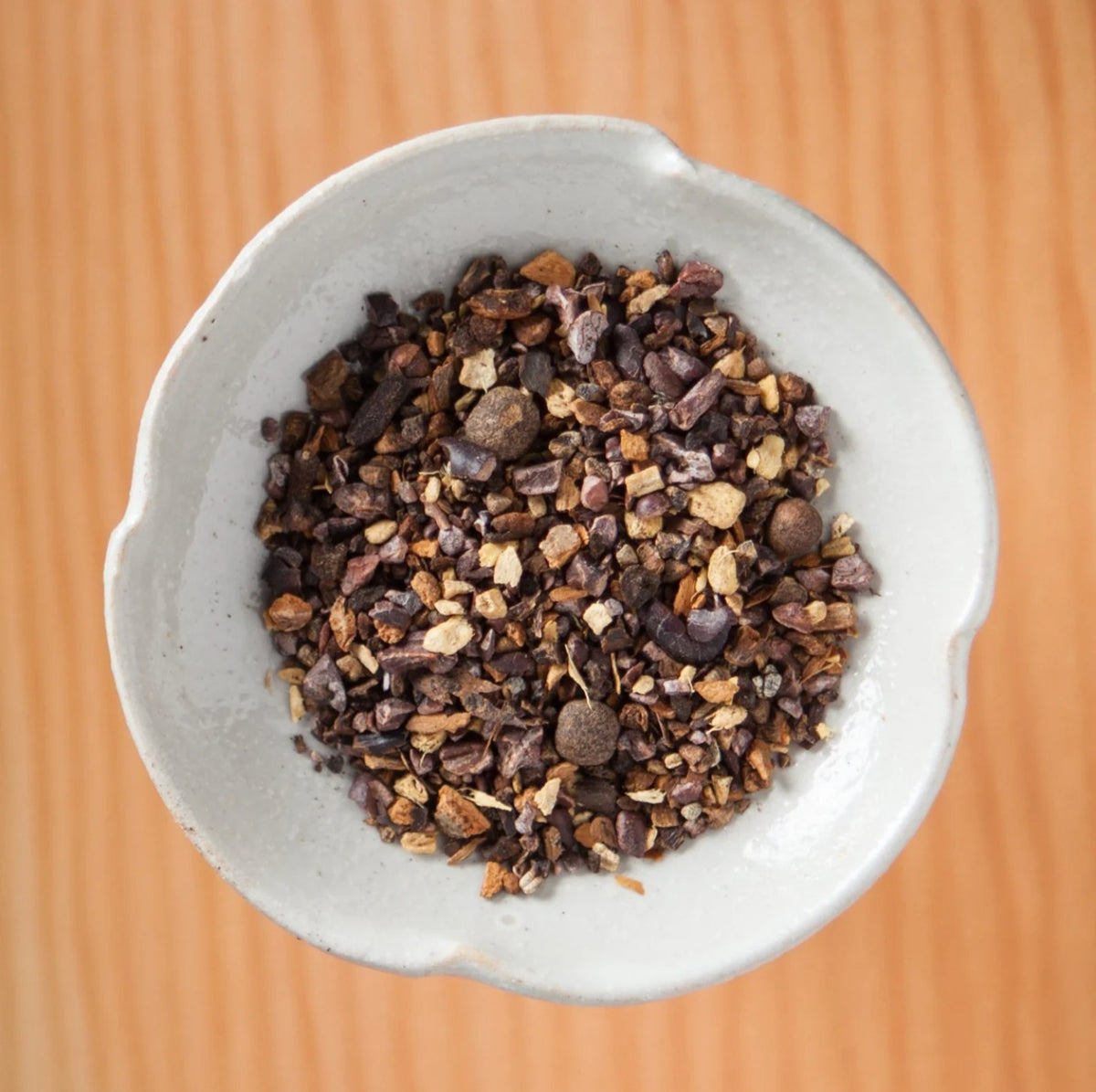 Dry Chokola tea blend in a bowl on a wooden table, showing the loose leaves and herbs inside the tea bags