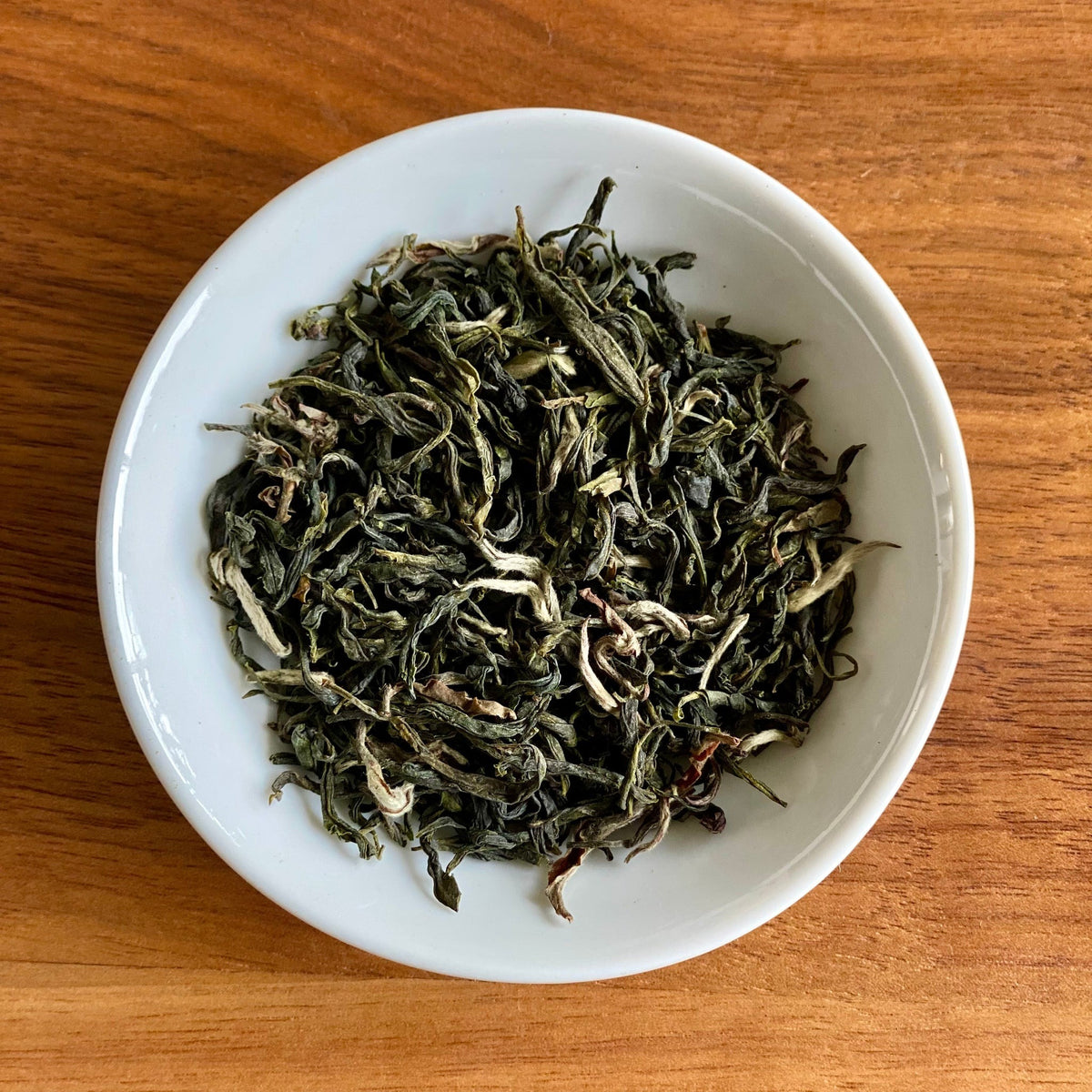 Dry Cloud Mountain tea blend in a bowl on a wooden table, showing the loose leaves and herbs inside the tea bags