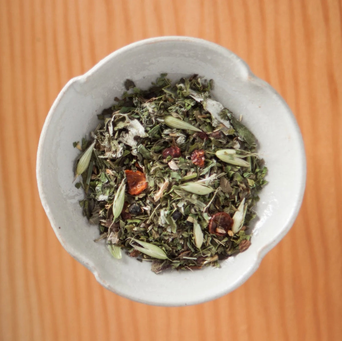 Dry Farm & Forest tea blend in a bowl on a wooden table, showing the loose leaves and herbs inside the tea bags