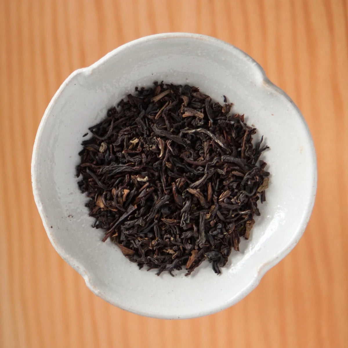 Dry Irish Breakfast tea blend in a bowl on a wooden table, showing the loose leaves and herbs inside the tea bags