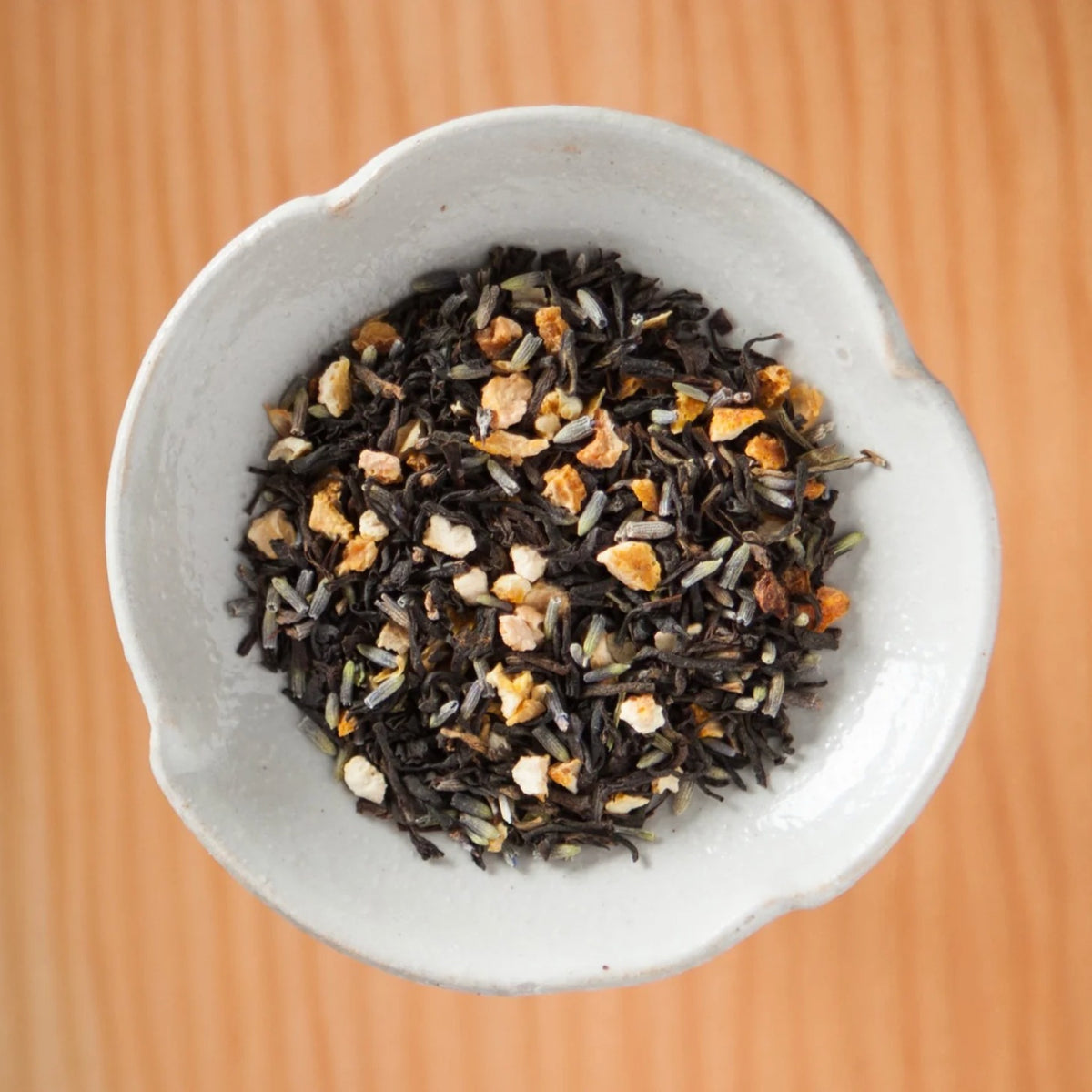 Dry Lavender Orange Grey tea blend in a bowl on a wooden table, showing the loose leaves and herbs inside the tea bags