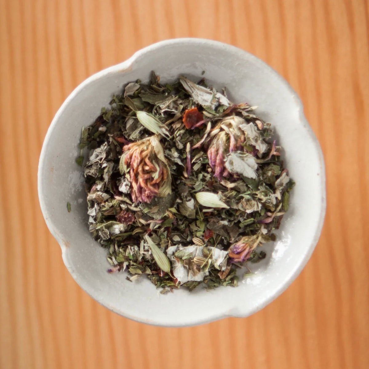 Dry Mama's Pregnancy tea blend in a bowl on a wooden table, showing the loose leaves and herbs inside the tea bags
