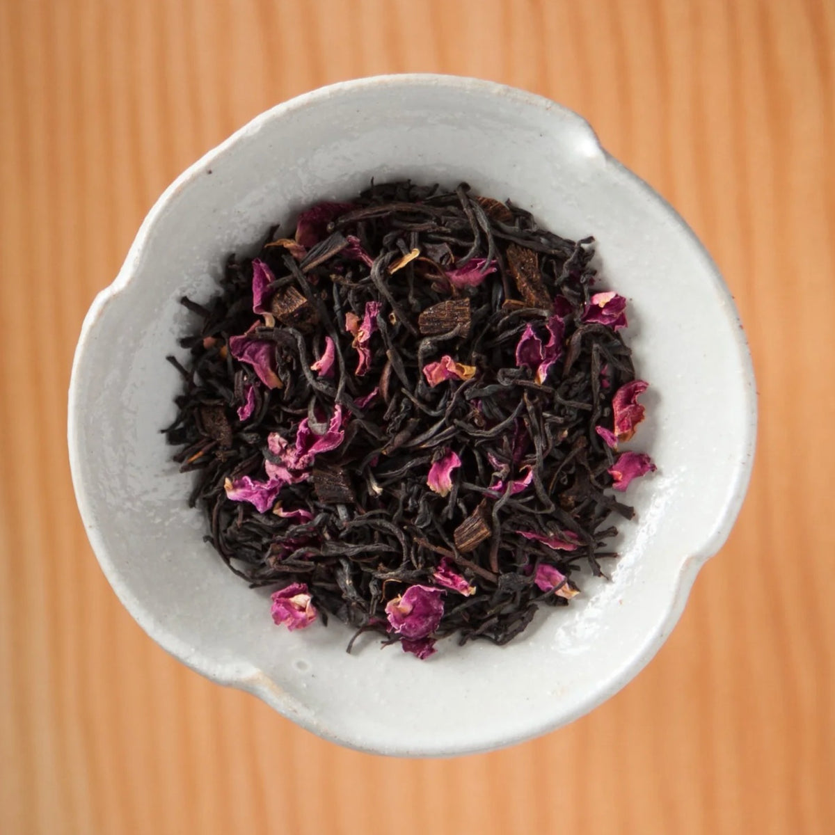 Dry Vanilla Rose Ceylon tea blend in a bowl on a wooden table, showing the loose leaves and herbs inside the tea bags