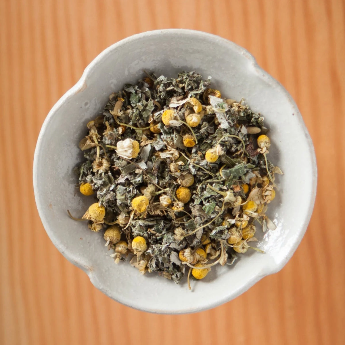 Dry Whatcom Chamomile tea blend in a bowl on a wooden table, showing the loose leaves and herbs inside the tea bags