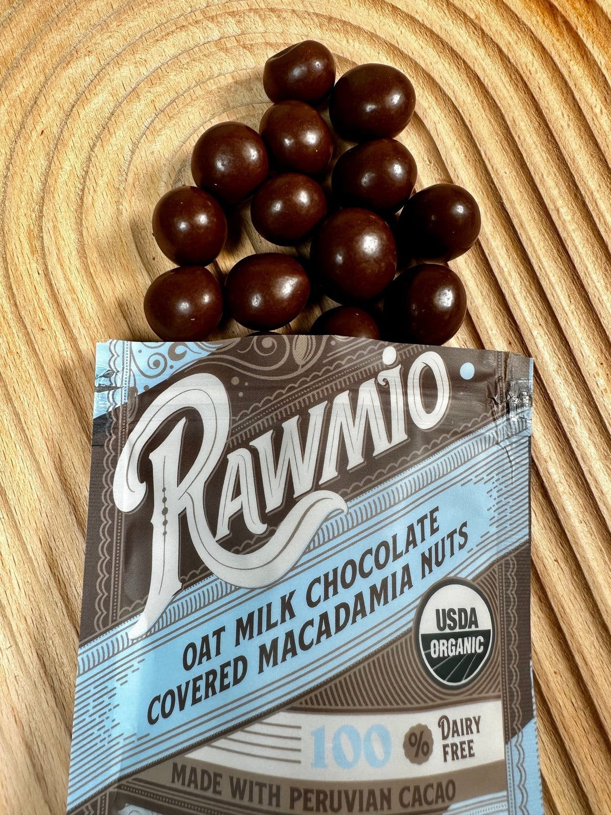 Windy City Organics Rawmio Oat Milk Chocolate Covered Macadamia Nuts styled on a table